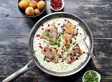 Sprøstekt fisk av sei i en panne med rømmesaus toppet med granateple og persille